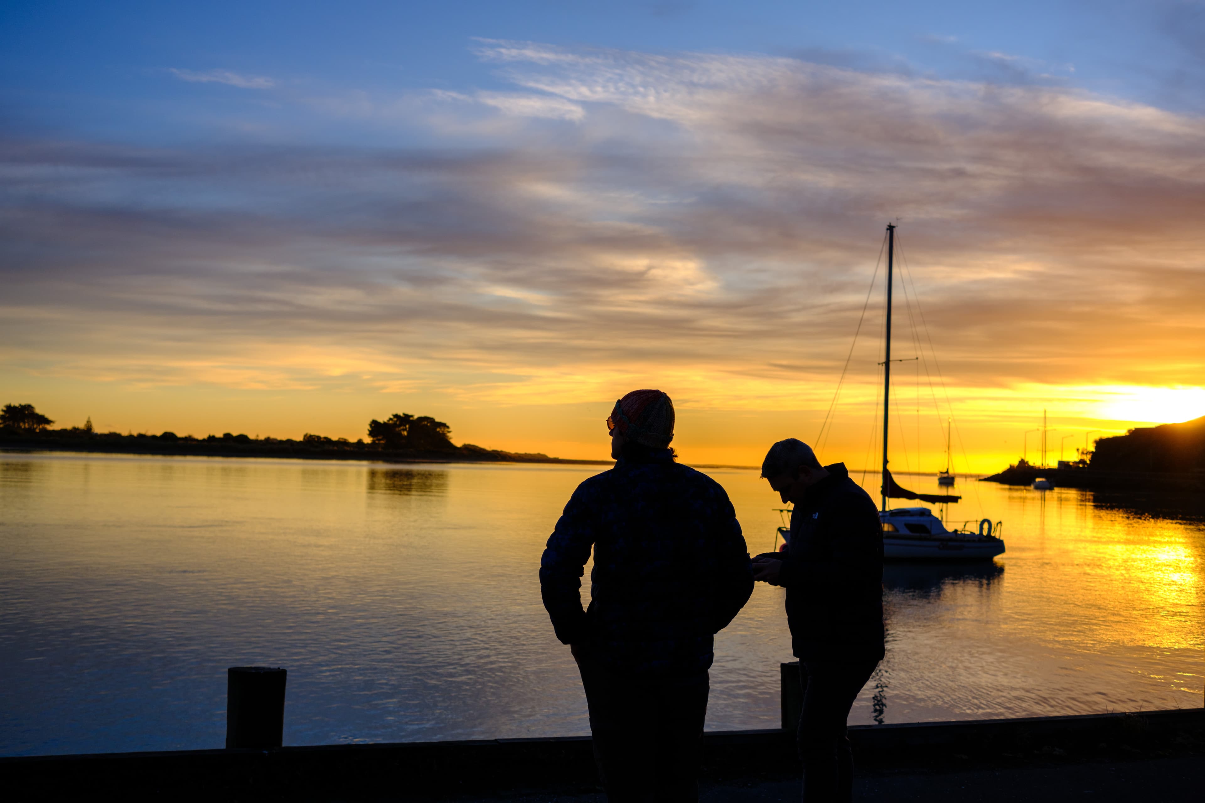 27mm · f/3.6 · 1/1250s · ISO 200
FUJIFILM X-T5 · XF27mmF2.8 R WR · May 24, 2024
Two silhouetted people watch a golden Christchurch sunrise by water.
Christchurch, New Zealand
© Brandon Cook