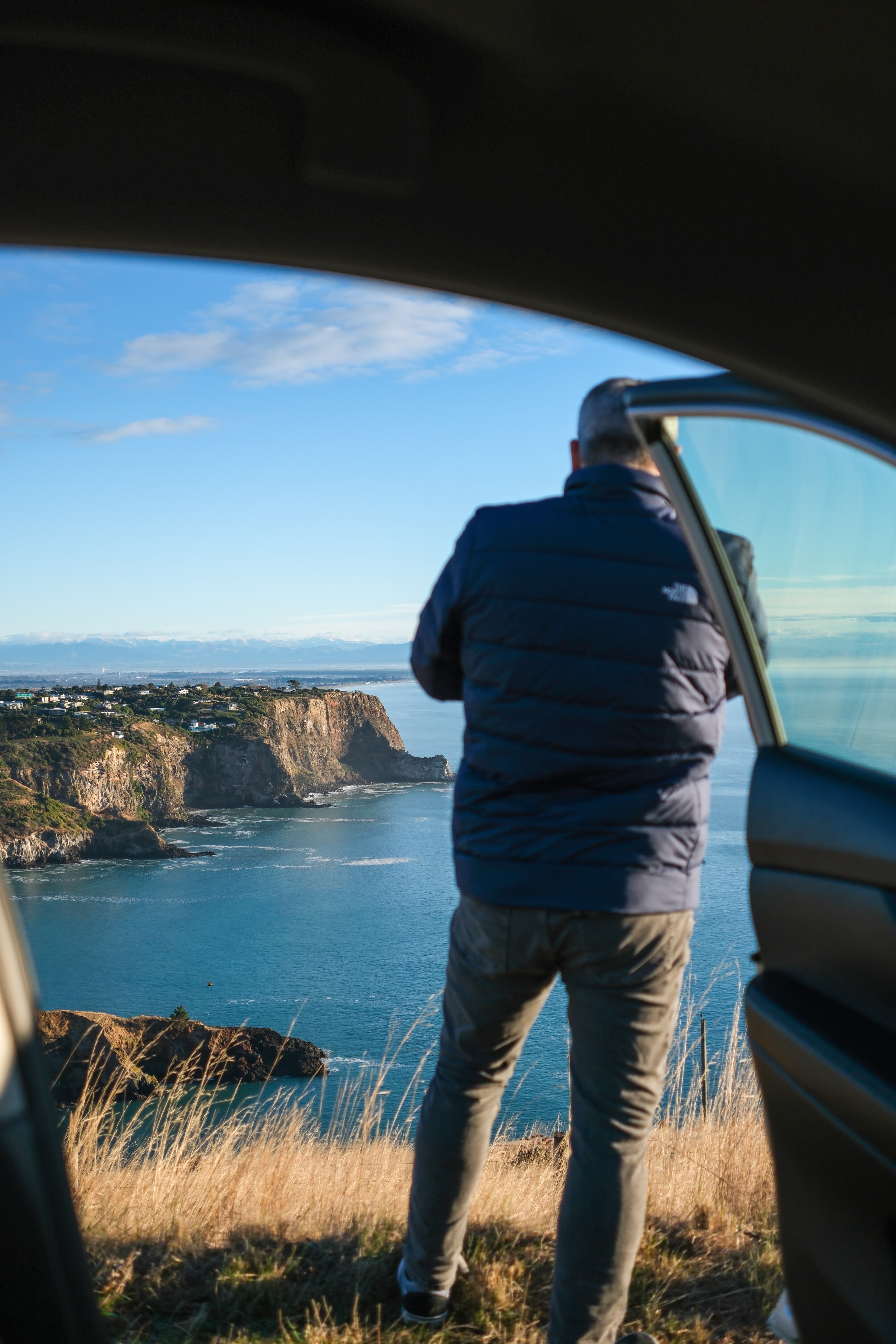 27mm · f/2.8 · 1/2500s · ISO 200
FUJIFILM X-T5 · XF27mmF2.8 R WR · May 24, 2024
Man viewing scenic Christchurch cliffs through an open car door.
Christchurch, New Zealand
© Brandon Cook